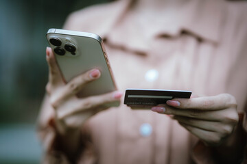 A woman holds a credit card and a smartphone, often shopping or conducting financial transactions online.