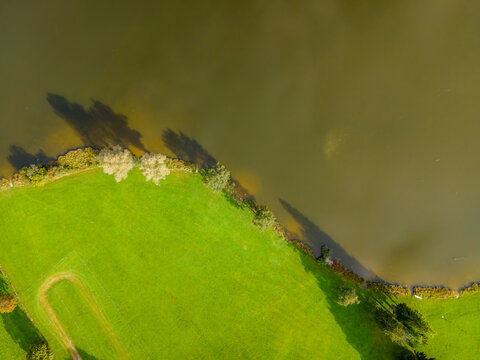 Aerial view of the vibrant green meadow meeting the still, dark waters of the lake, creating a striking contrast of color and texture, Ruckholz, Bayern, Germany.