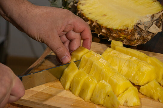 A freshly peeled pineapple is being sliced into chunks on a wooden cutting board