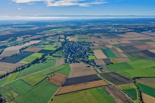 Aerial view of a patchwork quilt of vibrant green and brown fields stretching towards a quaint village nestled amidst trees under a vast sky, Rouffach, Grand Est, France.