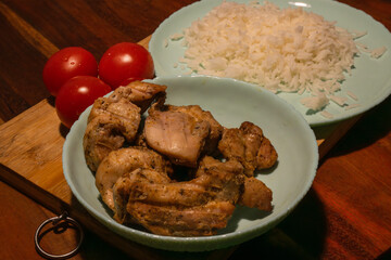 A simple, wholesome meal of rice, grilled chicken, and fresh tomatoes is arranged on a wooden surface 