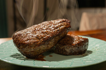 Steam rises from two freshly seared steaks on a patterned blue plate