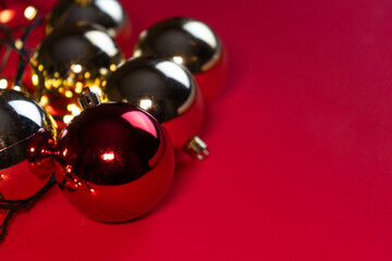 Christmas red and gold baubles lying on a bright red background with warm reflections and holiday lights. 