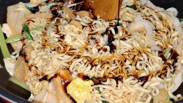 Close-up of noodles being drizzled with sweet soy sauce while preparing Chinese-style fried noodles.