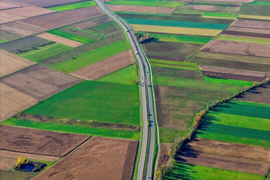 Aerial view of a long road cutting through a patchwork of vibrant green and earthy brown fields, creating a striking contrast in the rural landscape, Rouffach, Grand Est, France.
