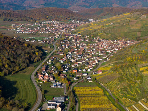 Aerial view of a charming town nestled between rolling hills, a tapestry of autumnal colors painting the landscape, Rouffach, Grand Est, France.