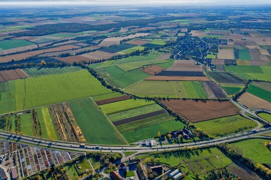 Aerial view of a patchwork of vibrant agricultural fields contrasting with the dark green of the distant forest, bisected by a modern highway, Rouffach, Grand Est, France.