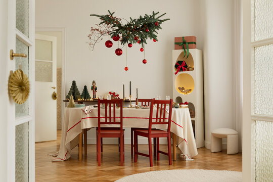 Bright dining room with a festive table setting and red chairs. Christmas decorations with natural greenery and ornaments.