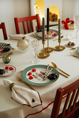 Close-up of an elegant Christmas table with candles, festive plates, and golden cutlery. Refined and joyful holiday styling.