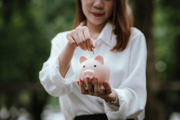 A woman wearing a white shirt is saving money by putting a coin into a pink piggy bank, symbolizing financial planning and saving for the future.