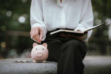 A woman wearing a white shirt is saving money by putting a coin into a pink piggy bank, symbolizing financial planning and saving for the future.
