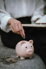 A woman wearing a white shirt is saving money by putting a coin into a pink piggy bank, symbolizing financial planning and saving for the future.