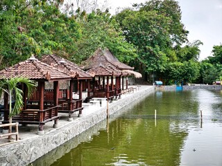 Gazebo on the edge of the pond where the water reflects the shadows of the surrounding shady trees