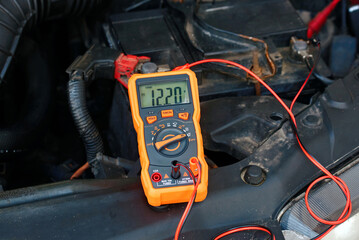 Voltage measurement on vehicle battery, diagnostic test, electrical maintenance process. Auto repair scene with multimeter connected to battery posts showing 12.20 volts during service inspection