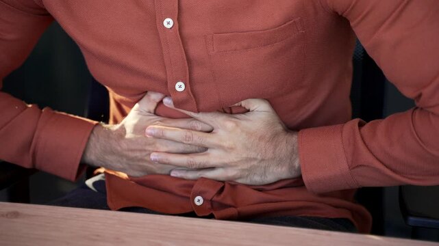 Close up. Male hands holding massaging stomach. Businessman in shirt feels stomach pain sitting at workplace in business office. Sick man worker suffers from gastritis, poisoning or bloating