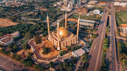Aerial view of the National Mosque casting a golden hue amidst the city's lush greenery and structured roads, Abuja, Federal Capital Territory, Nigeria.