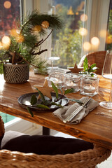 Atmospheric christmas table decoration in a cozy conservatory with festive bokeh lights. Romantic christmas dinner concept with lit candles in a restaurant. Vertical gastronomy background.