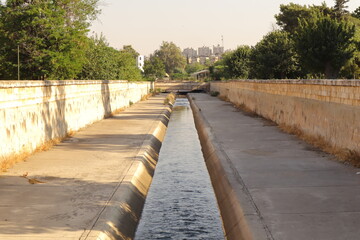 Peaceful view of the Queiq River running through Al-Shahba Public Garden in Aleppo, Syria. This urban nature scene highlights the harmony between water, greenery and city life. Travel, environmental.