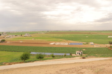 Panoramic view of the fertile plains of Marj Dabiq near Aleppo, Syria, showing green farmlands and solar panels under cloudy skies. Useful for topics on agriculture, renewable energy, rural landscapes
