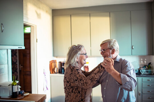 Senior husband and wife dancing joyfully in home kitchen
