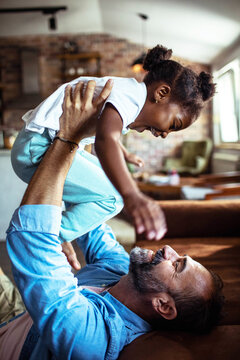 Happy adult father lifting laughing child daughter at home