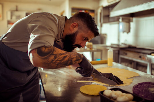 Adult man chef concentrating while slicing dough in commercial kitchen