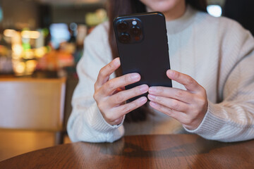 Closeup image of a woman holding and using mobile phone while drinking coffee in cafe