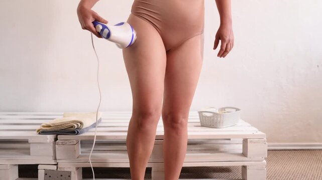 A woman massages problem areas, thighs, and buttocks, to combat cellulite. Anti-cellulite home treatment, lymphatic drainage with a handheld electric massager. no face