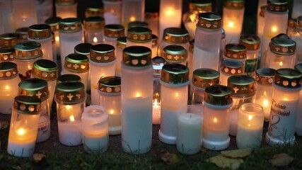 Burning candles placed on graves in a quiet cemetery, warm flickering flames illuminating headstones and creating a peaceful memorial atmosphere, captured in 4K ultra HD.