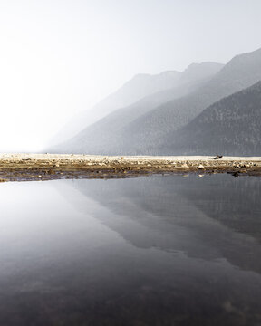 View of mountains fading into a misty horizon reflected on the still water, creating a serene and ethereal landscape, Vancouver, British Columbia, Canada.