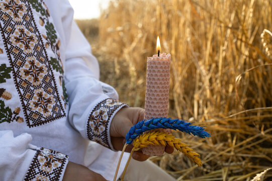 candle, yellow blue ears of wheat, held by boy wearing Ukrainian embroidered shirt, stands in wheat field. Conceptual photo, commemorating the Holodomor in Ukraine. Genocide Remembrance Day.