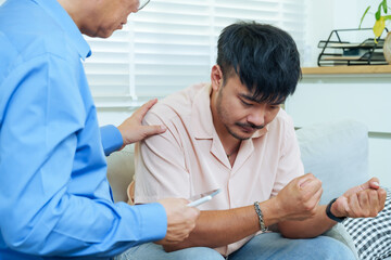 Obraz premium Asian adult man sitting on sofa during psychological consultation with male therapist in blue shirt, expressing anxiety and frustration while seeking professional mental health advice in modern clinic