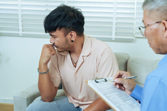Asian man covering face and clenching fists while talking to psychiatrist, expressing deep sorrow and frustration, seeking emotional release, mental support, psychological healing in therapy session