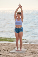 Young woman practicing mindfulness yoga exercise on Baltic Sea beach at sunrise