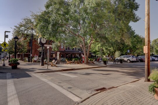 View of crosswalk lines cutting through asphalt streets leading to restaurants and shops shaded by green trees in Loveland, Ohio, United States, Loveland, Ohio, United States.