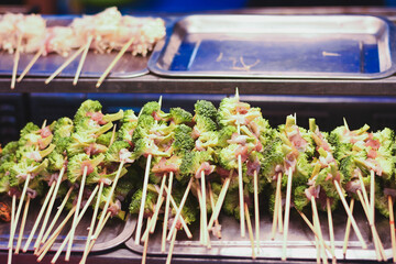 Broccoli and meat skewers arranged on metal trays for grilling.
