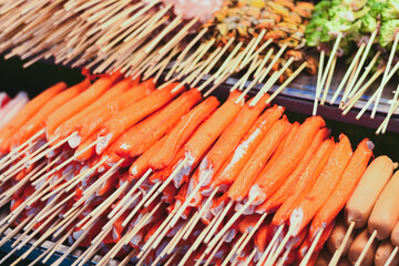 Many bright orange crab sticks on skewers at a food stall.