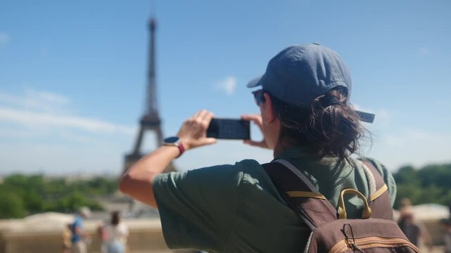 Woman tourist taking a picture of the eiffel tower with a smartphone on a sunny day in paris, enjoying city break travel and sightseeing experience