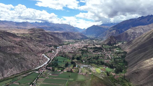 Moving forward shot captures the green agricultural plots and dense housing of the remote Yucay area under a bright sky