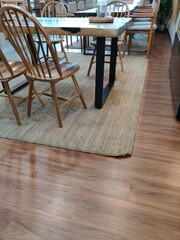 Interior scene featuring a wooden dining table with matching chairs on a woven rug, placed over polished wooden flooring in a warm, cozy setting