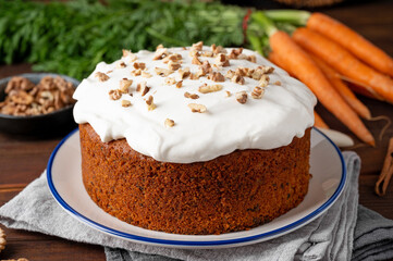 Carrot cake with cinnamon, walnuts and cream cheese frosting on a plate on a dark wooden background. Rustic style. Copy space.