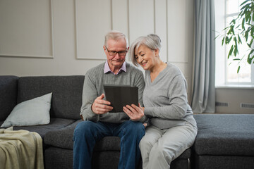 Senior old couple with tablet watching video online. Husband wife spending time together at home. Happy modern mature senior couple using tablet for family entertainment. Old people modern technology