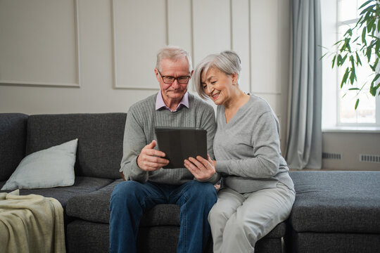 Senior old couple with tablet watching video online. Husband wife spending time together at home. Happy modern mature senior couple using tablet for family entertainment. Old people modern technology