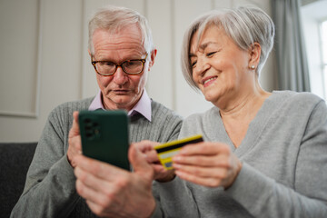 Senior couple man woman shopping online with smartphone paying with credit card. Old people buying on Internet enter credit card details at home indoors. Online shopping delivery service ecommerce