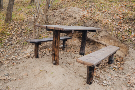 wooden table and benches for recreation in an autumn park with dry leaves and sand on the ground