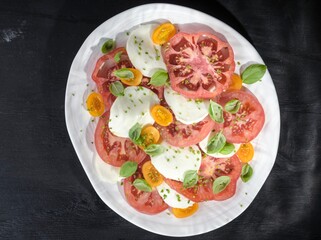 Fresh mozzarella sits atop vibrant tomato slices, garnished with basil and yellow cherry tomatoes, creating an inviting salad in a sunlit garden setting during a warm afternoon
