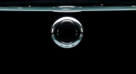A single transparent bubble floating in water against a stark black background in close up view