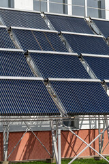 A large installation of evacuated tube solar water heaters mounted on a frame. These panels collect thermal energy from the sun to heat water for a swimming pool, promoting energy saving and autonomy.