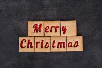 Holiday square cookies with red, marmalade filling in the shape of the words Merry Christmas. Dark background. Top view.