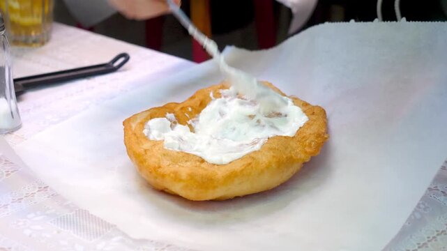 Hands seasoning traditional Krumplis Langos with sour cream and cheese